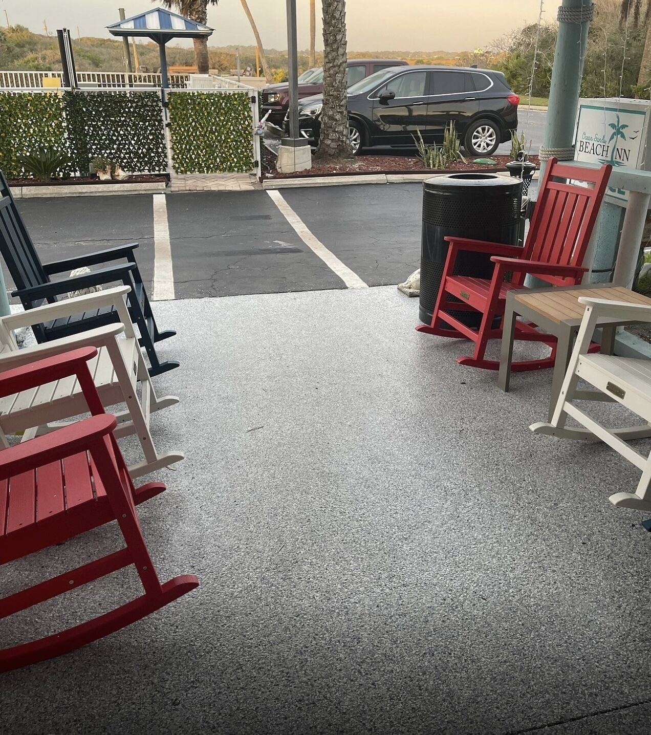 A covered outdoor seating area with red and white Adirondack chairs, a trash bin, and a sign for Beach Inn.