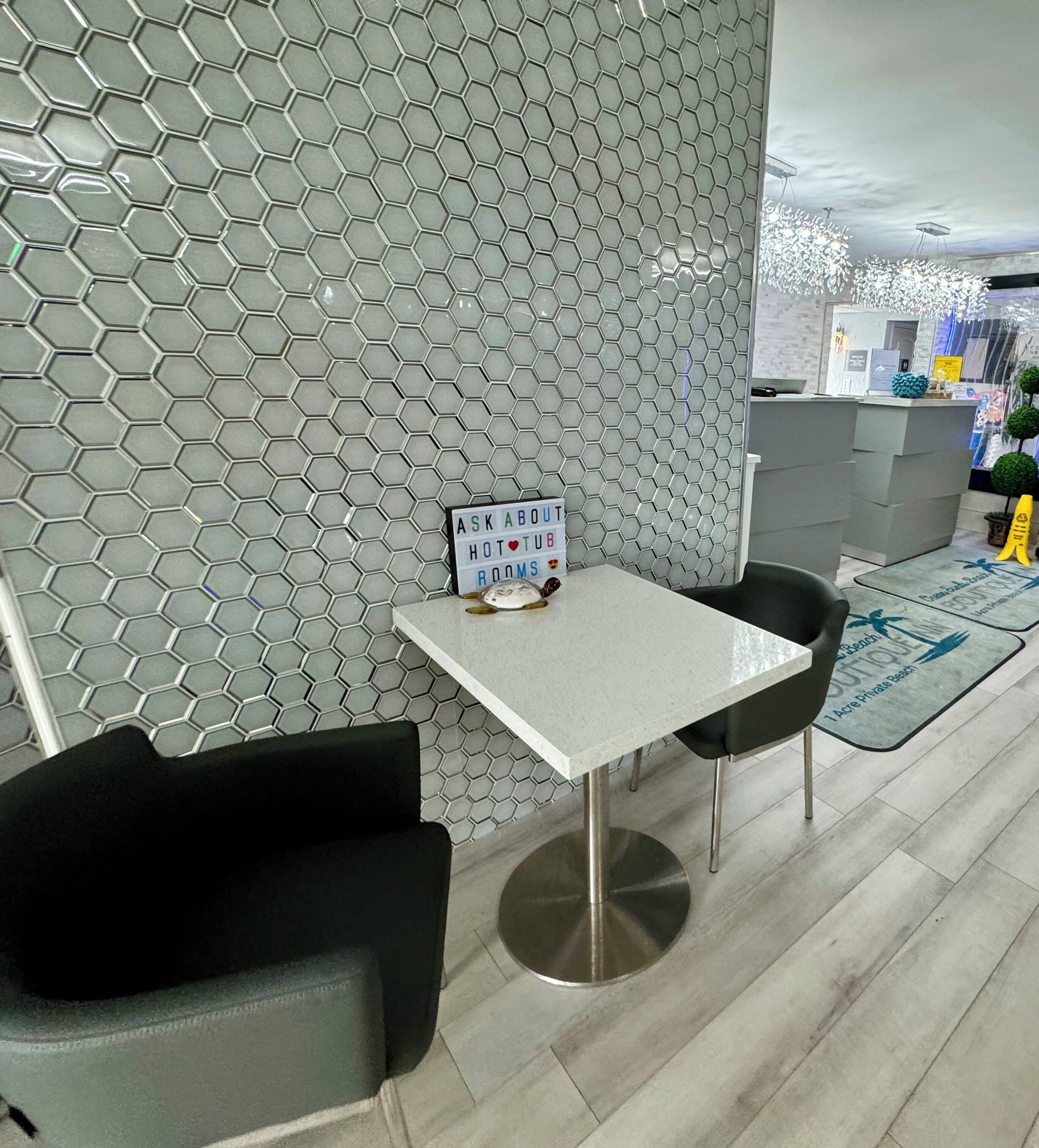 Un interior moderno con un revestimiento mural de patrón hexagonal, una pequeña mesa con un letrero y sillas negras.