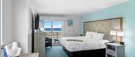Quarto de hotel com cama, mesa de cabeceira, cadeira, escrivaninha e vista para o mar.