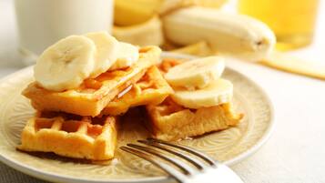 Um prato de waffles coberto com fatias de banana e um copo de leite ao fundo.