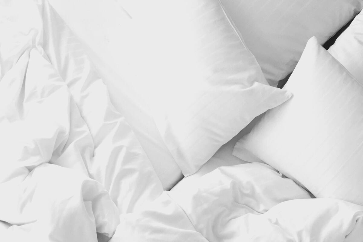 Uma cama com roupa de cama e almofadas brancas.