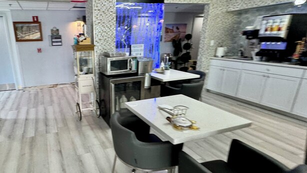 A modern kitchen with white cabinets, a microwave, and a coffee machine. There is a dining area with a white table and black chairs. - Ocean Sands Beach Boutique Inn - 1 Acre Private Beach (St. Augustine)