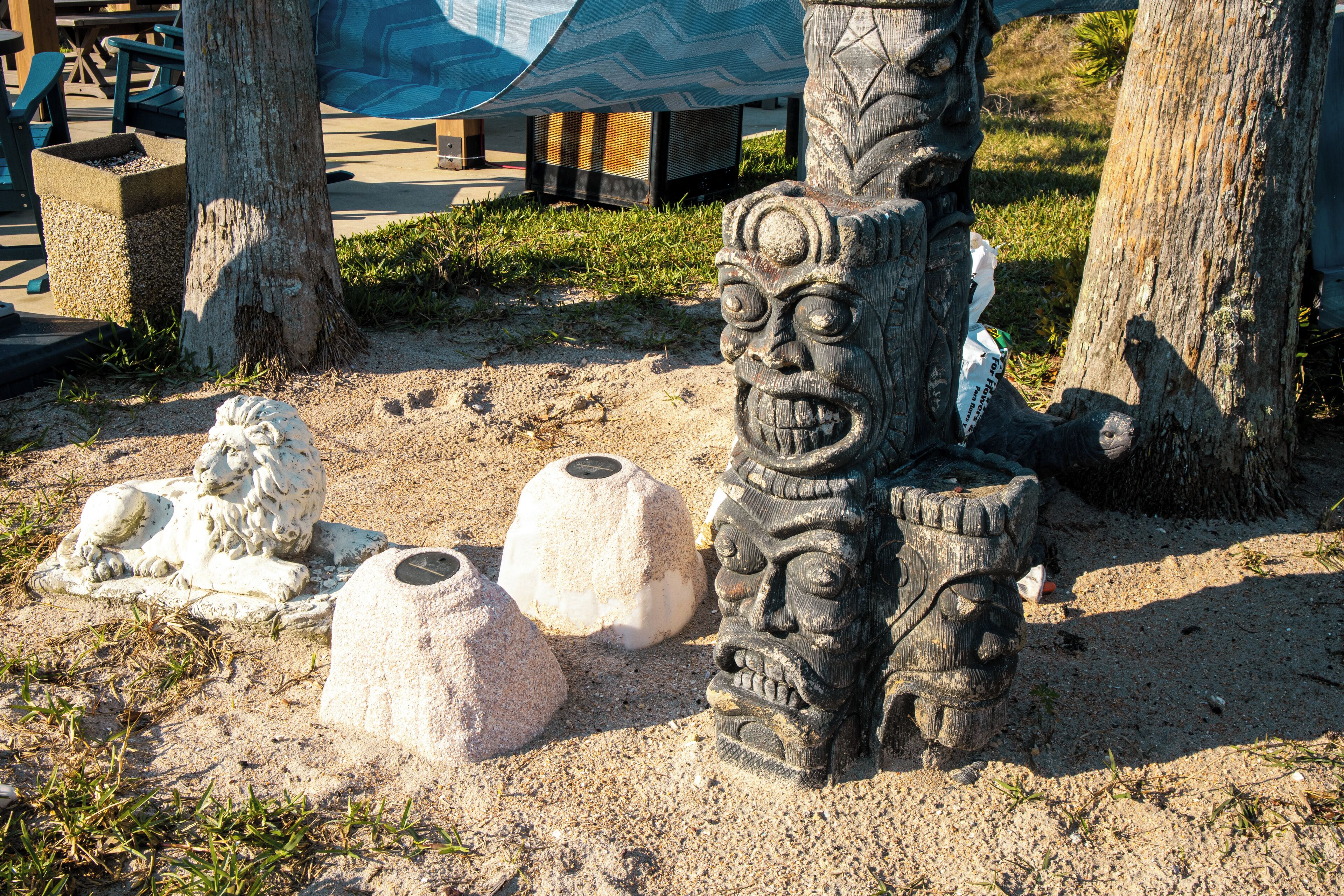 A sandy area with a stone sculpture of a face, a stone sculpture of a lion, and a stone sculpture of a bird.