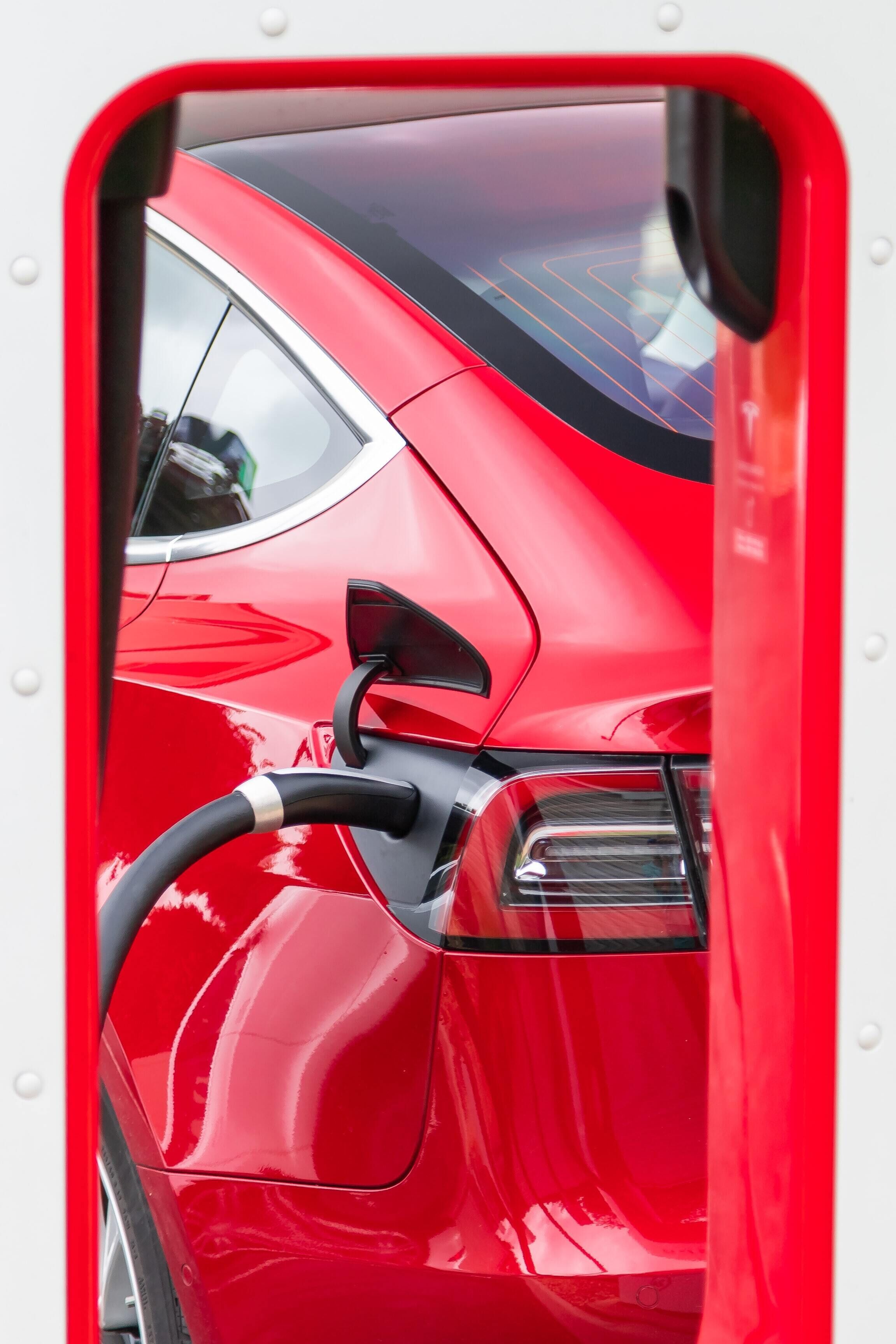 A red car with a charging cable connected to its port.