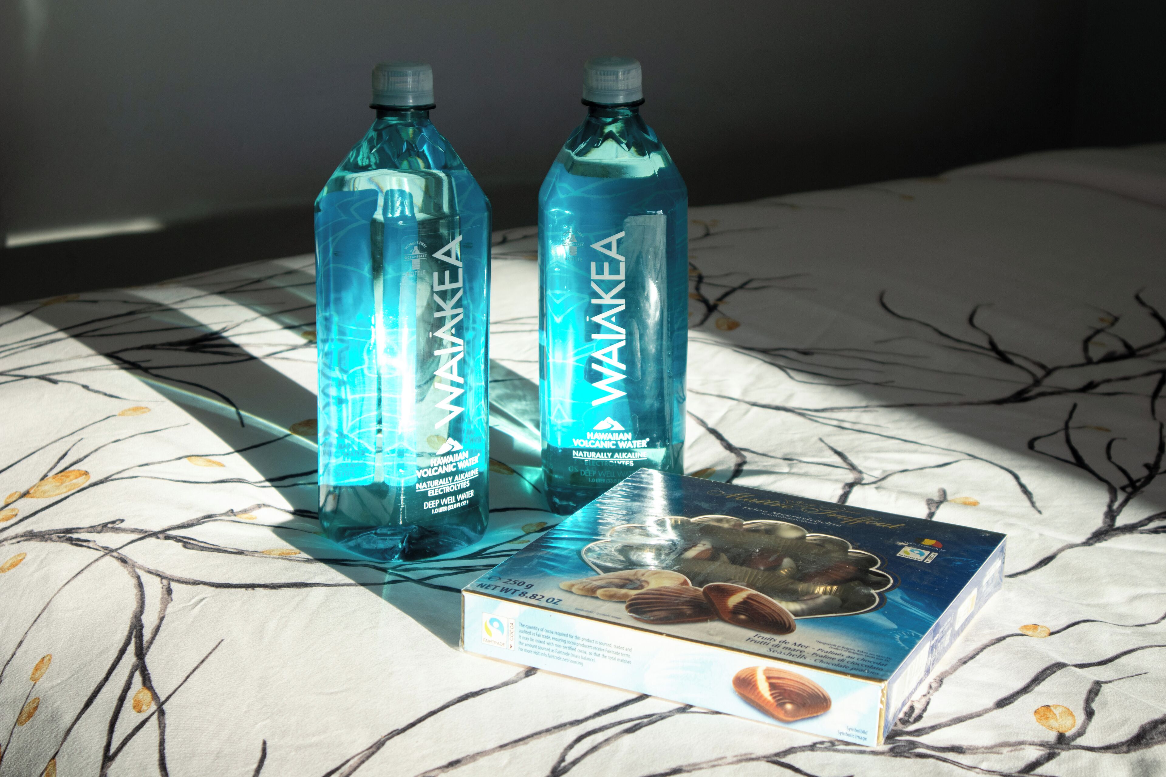 Dos botellas de agua volcánica hawaiana sobre una cama con un edredón estampado.