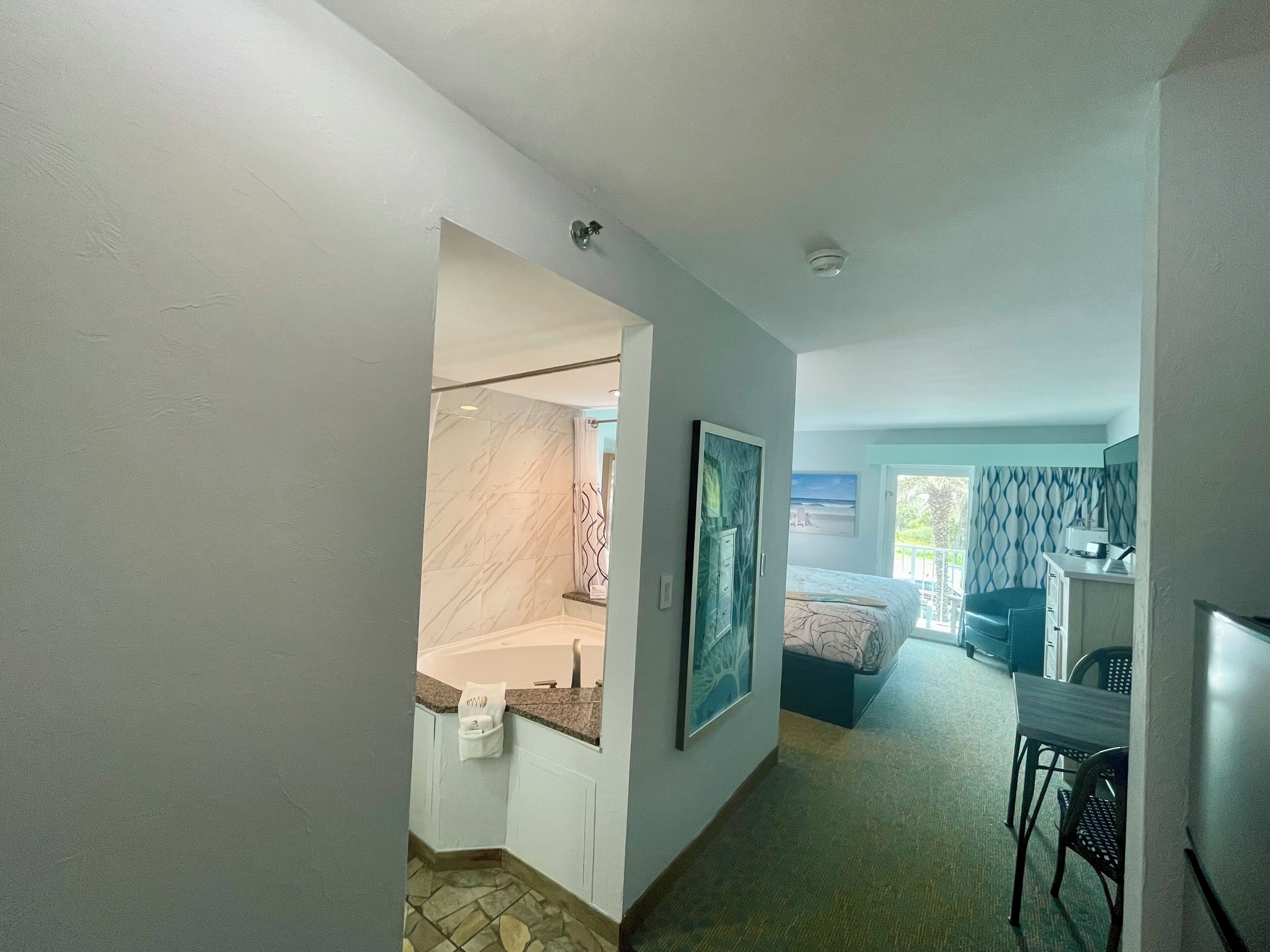 A hotel room with a bathroom, a bed, a desk, and a chair.