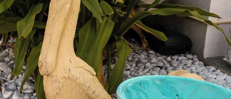 A garden with a bird sculpture and a turquoise birdbath surrounded by pebbles and green foliage.