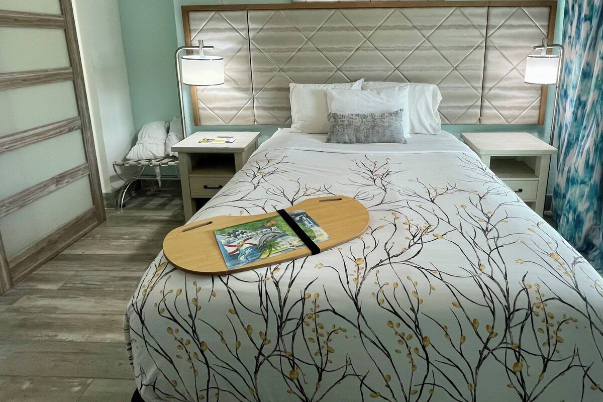 Quarto de hotel com uma cama, duas mesas de cabeceira, um criado-mudo, uma guitarra de madeira e uma janela com cortinas.