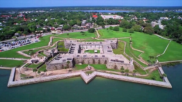 An aerial view of a historic fort with a moat, surrounded by greenery and a small town in the background.