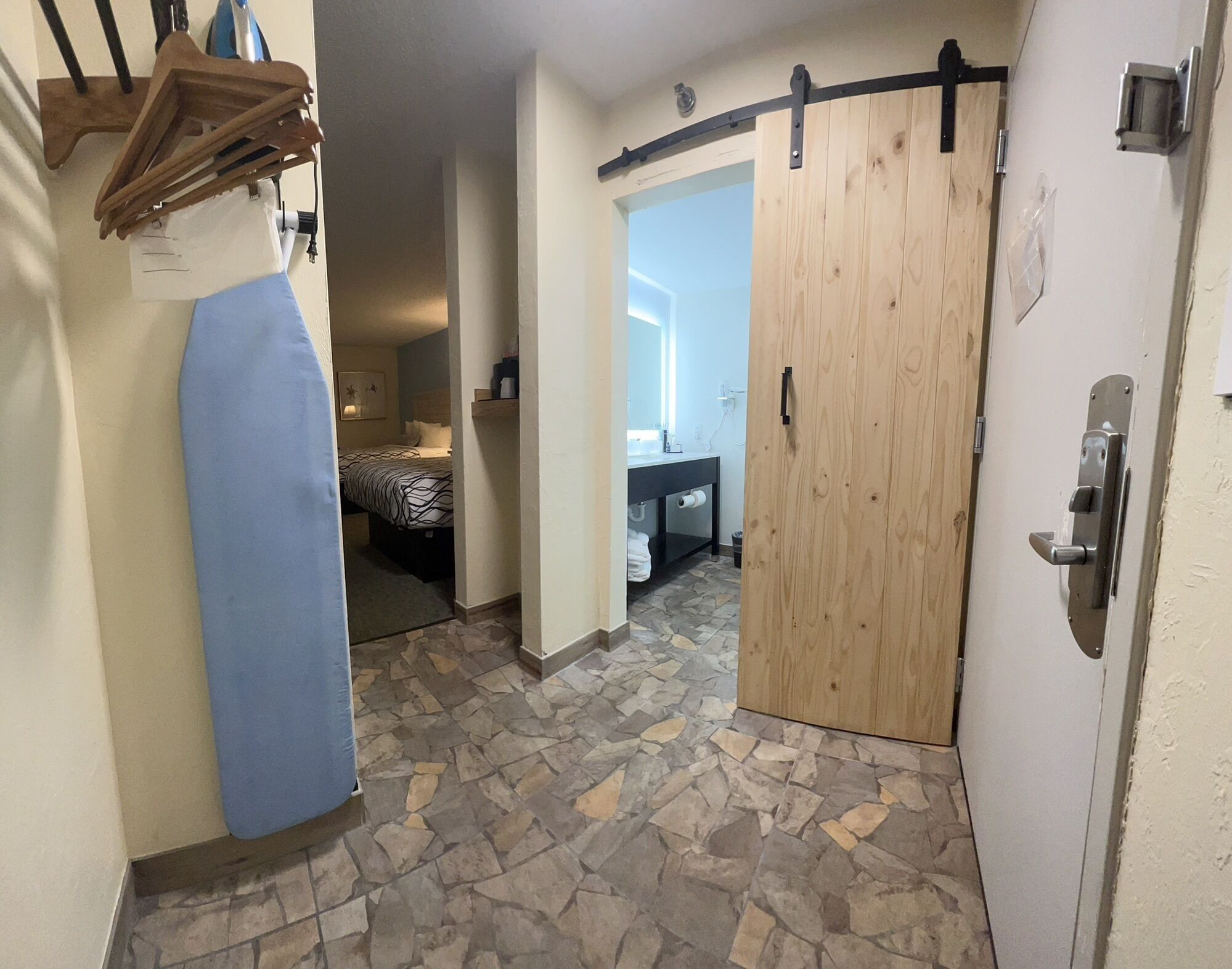 Una habitación con suelo de baldosas de piedra, una puerta de madera y una cama con colcha estampada.