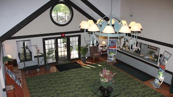 Een hotellobby met een groen tapijt met patroon, een receptiebalie, een kroonluchter en een groot raam met uitzicht op het omliggende landschap.