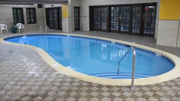 Una piscina interior con suelo a cuadros, una escalera y una puerta que da a otra habitación.