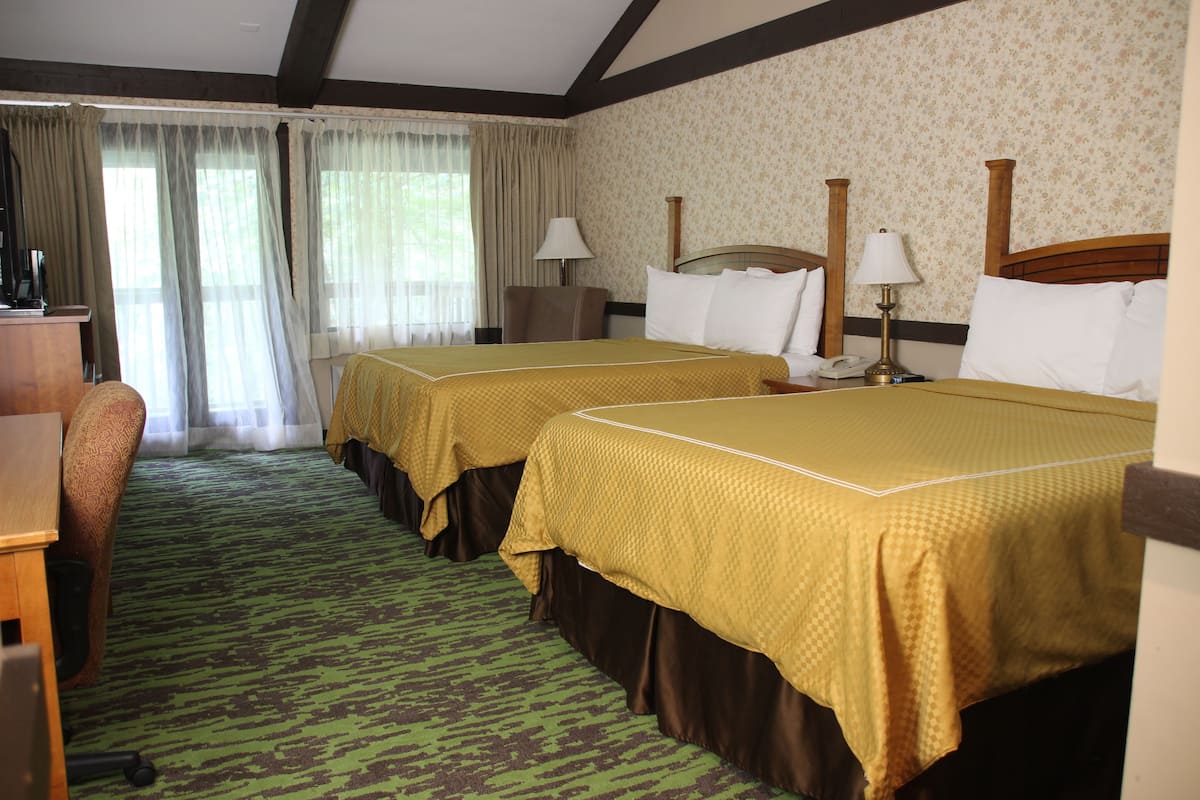 A hotel room with two beds, a desk, a chair, and a window with curtains.