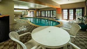 A pool area with a round table and chairs, a tiled floor, and large windows.
