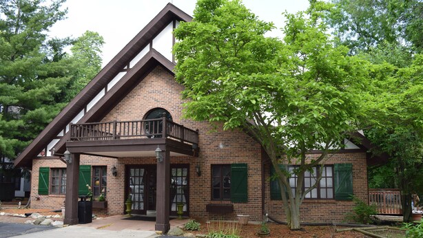 A brick building with a balcony and green shutters, surrounded by trees.