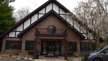 A two-story building with a brick facade, a balcony, and a car parked in front.