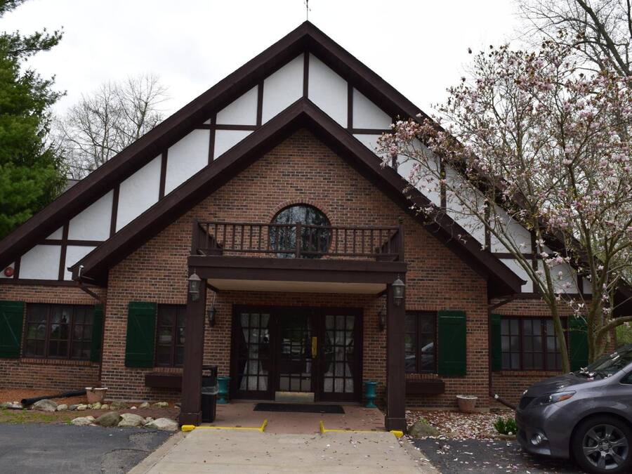 A two-story building with a brick facade, a balcony, and a car parked in front.