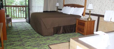 A hotel room with a large bed, a wooden nightstand with a lamp, a bathroom with a bathtub, and a view of greenery through the window.