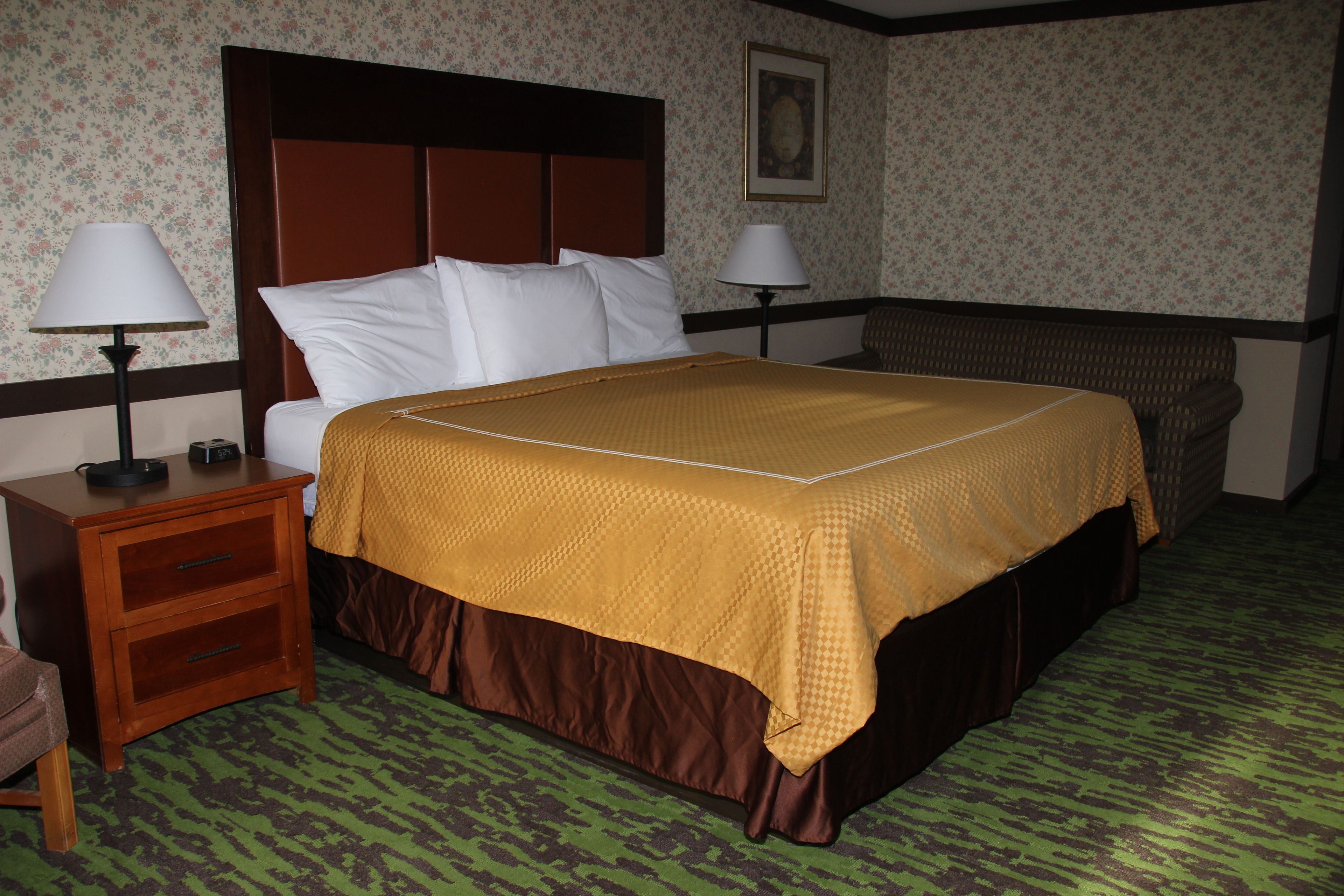 A hotel room with a bed, two bedside tables, a nightstand, a chair, a lamp, and a painting on the wall.