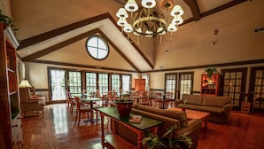 A spacious room with wooden floors, a large chandelier, and a cozy seating area with sofas and chairs.