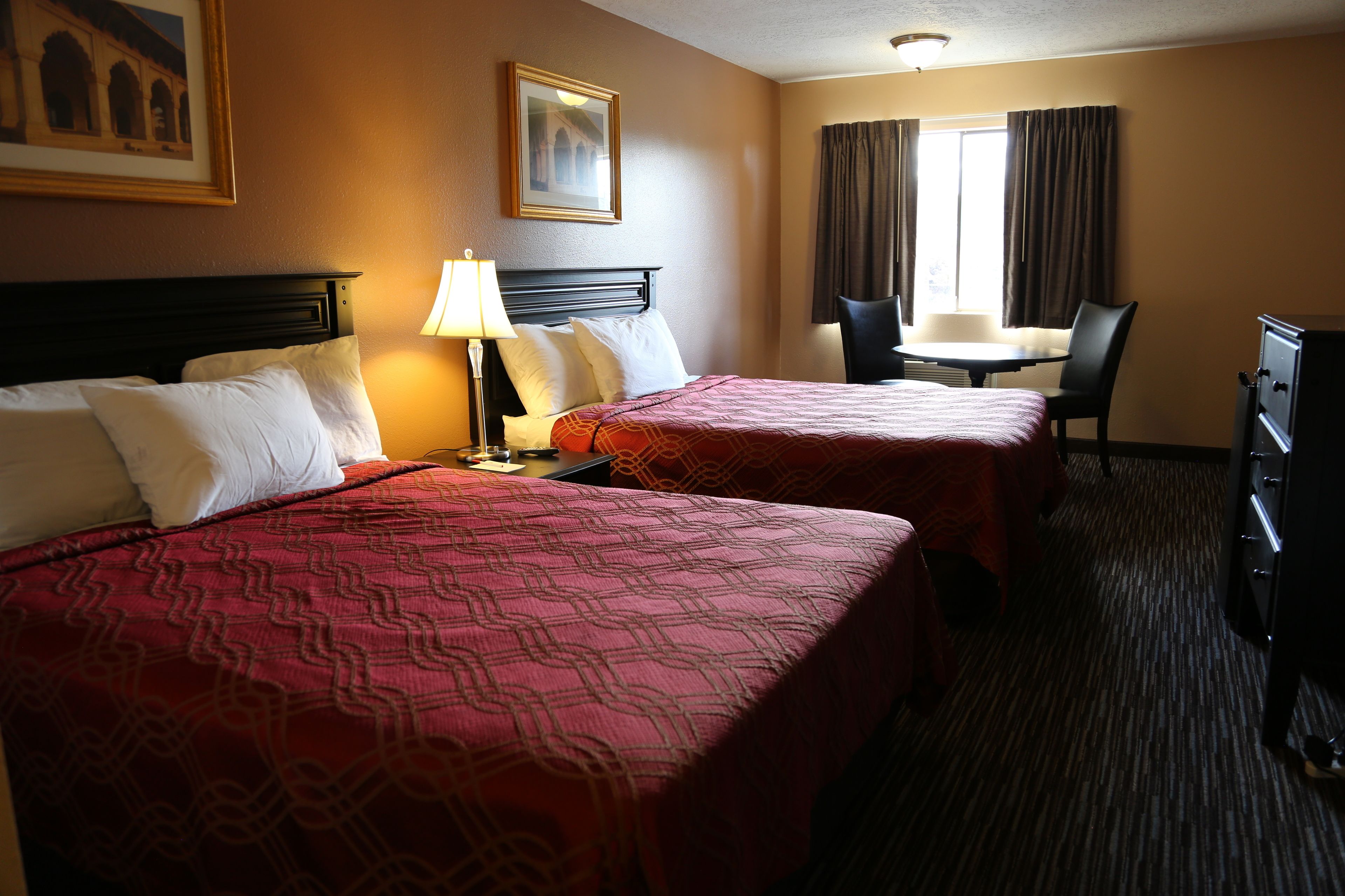 A hotel room with two beds, a desk, a chair, and a window with curtains.