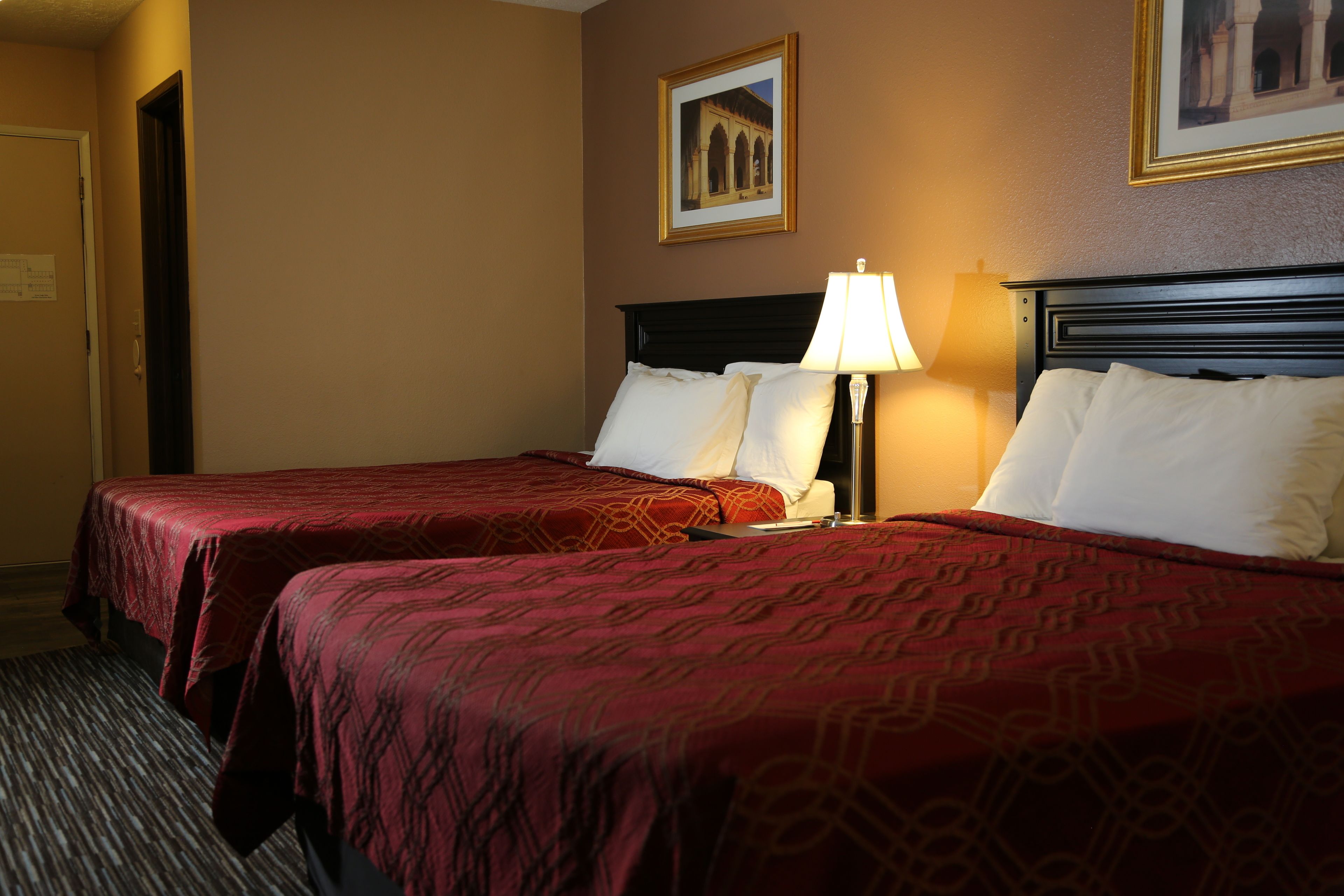 A hotel room with two beds, a nightstand with a lamp, and a framed picture on the wall.