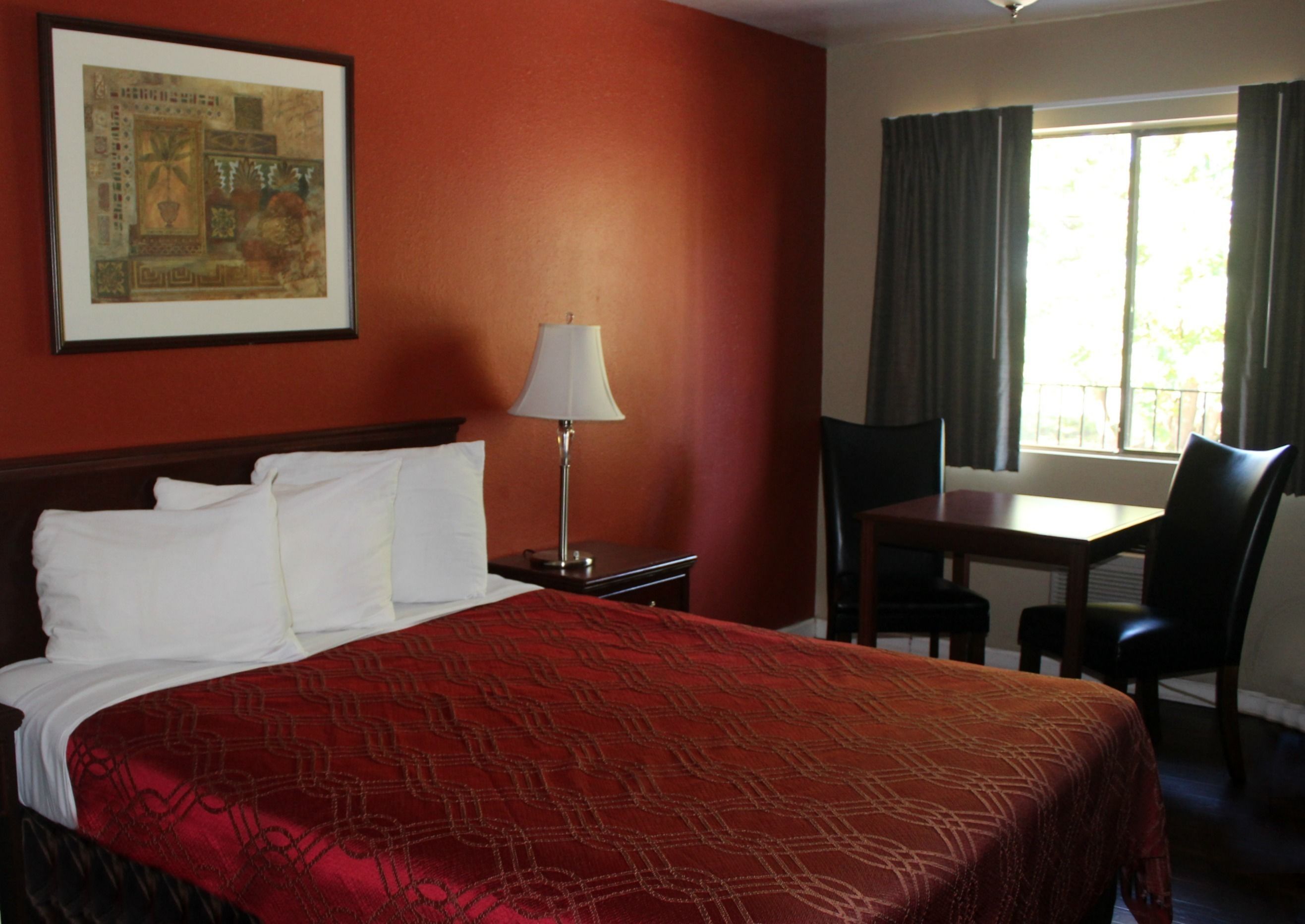 A hotel room with a bed, a desk, a chair, a lamp, and a window with curtains.