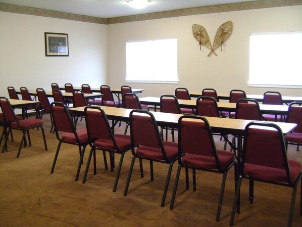 Un salón de conferencias con varias mesas y sillas, ventanas amplias y un cuadro en la pared.