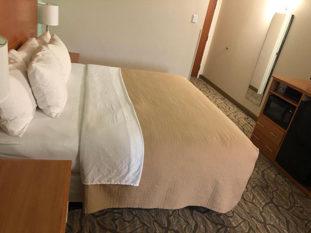 Ein Hotelzimmer mit einem Bett, einem Nachttisch aus Holz, einer Lampe, einem Spiegel und einem Fernseher.
