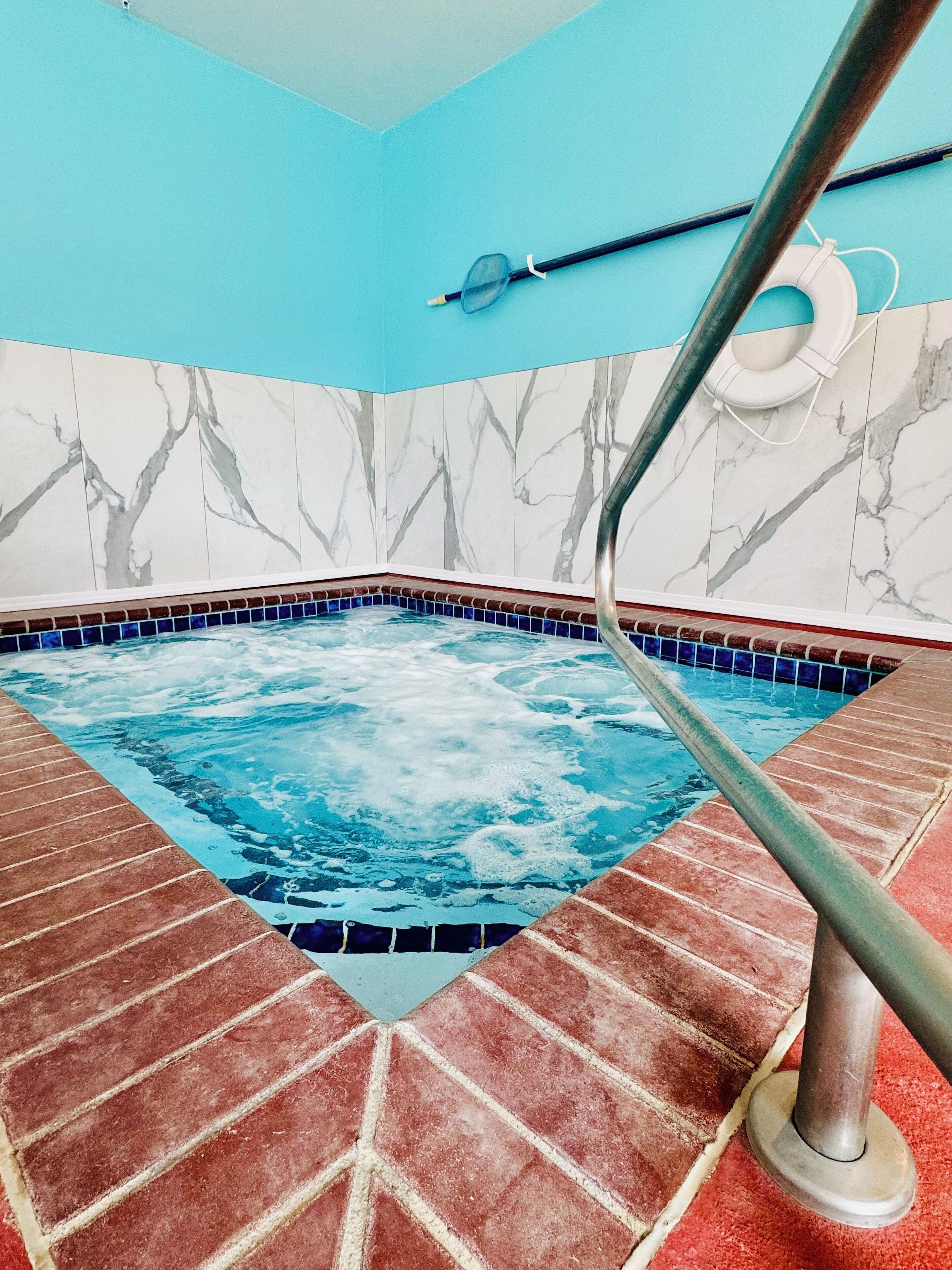 Un bain à remous doté d’un sol en mosaïque bleue, entouré de carreaux de briques rouges et de murs en marbre ornés d’un motif d’arbre.