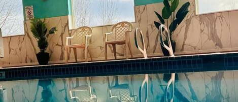 A pool area with two chairs and a potted plant.