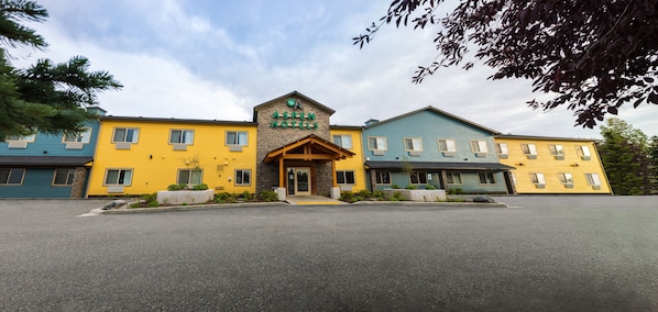 A hotel with a central entrance, multiple windows, and a parking lot.