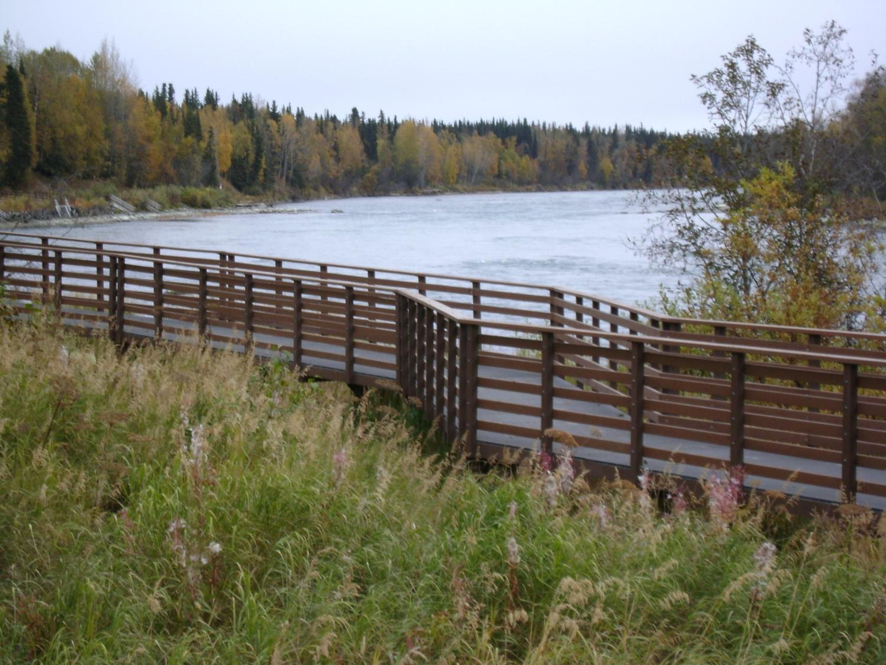 A wooden bridge over a river with a forested background.