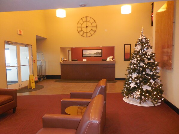 Un área de recepción con un árbol de Navidad, asientos de cuero, un reloj y una mesa de recepción.