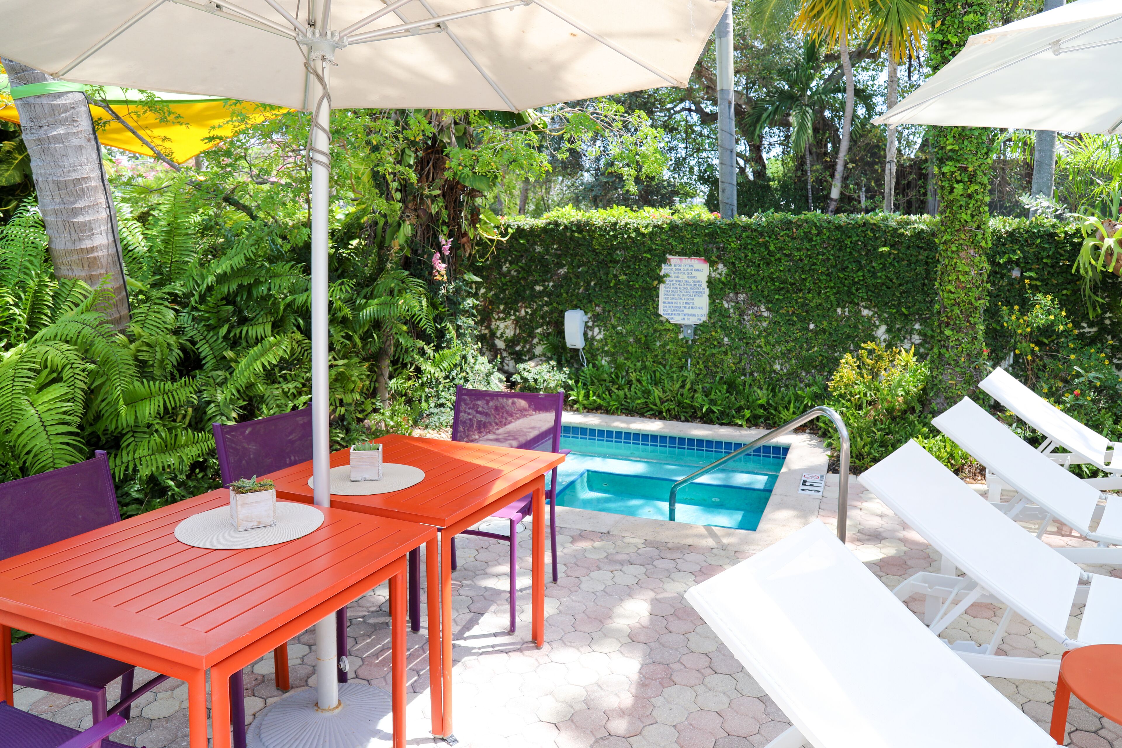 Un espace extérieur avec une piscine, une table et des chaises, le tout entouré d’une végétation luxuriante et d’une haie.