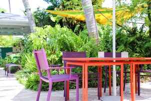 An outdoor seating area with a table and chairs, surrounded by lush greenery and a yellow canopy.