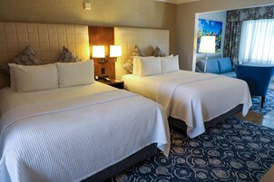 Una habitación de hotel con dos camas, una mesita de noche con lámpara, una silla y una alfombra estampada.