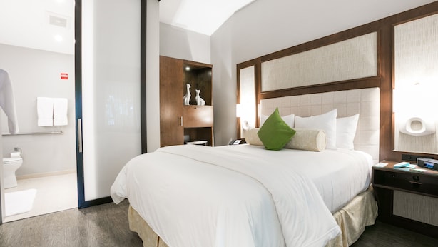 A modern hotel room with a large bed, a nightstand, a bedside table, and a bathroom visible through an open door. - Almond Tree Inn Hotel - Adults Only (Key West)