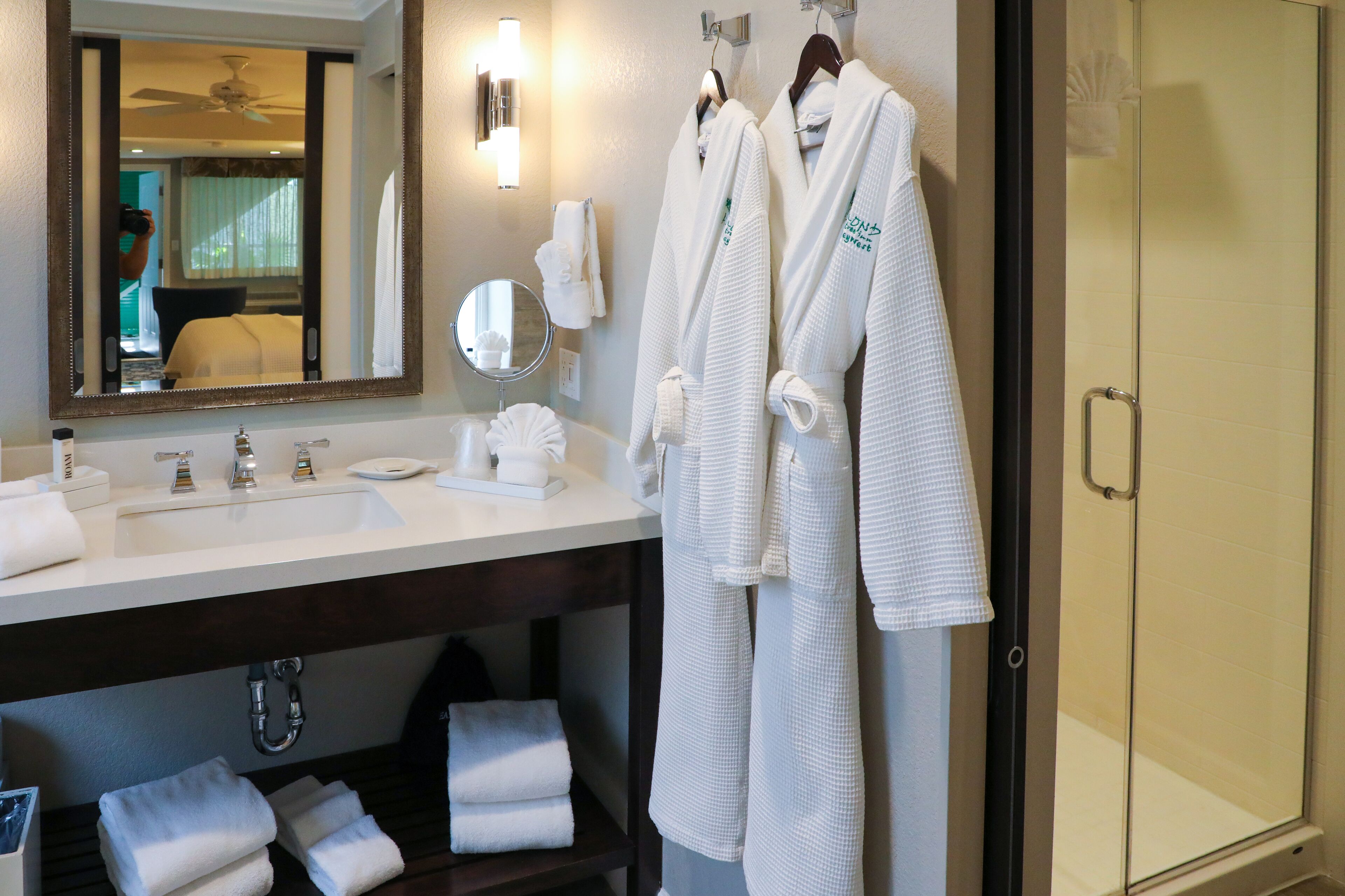 A hotel bathroom with a sink, mirror, towel rack, and a glass shower door.