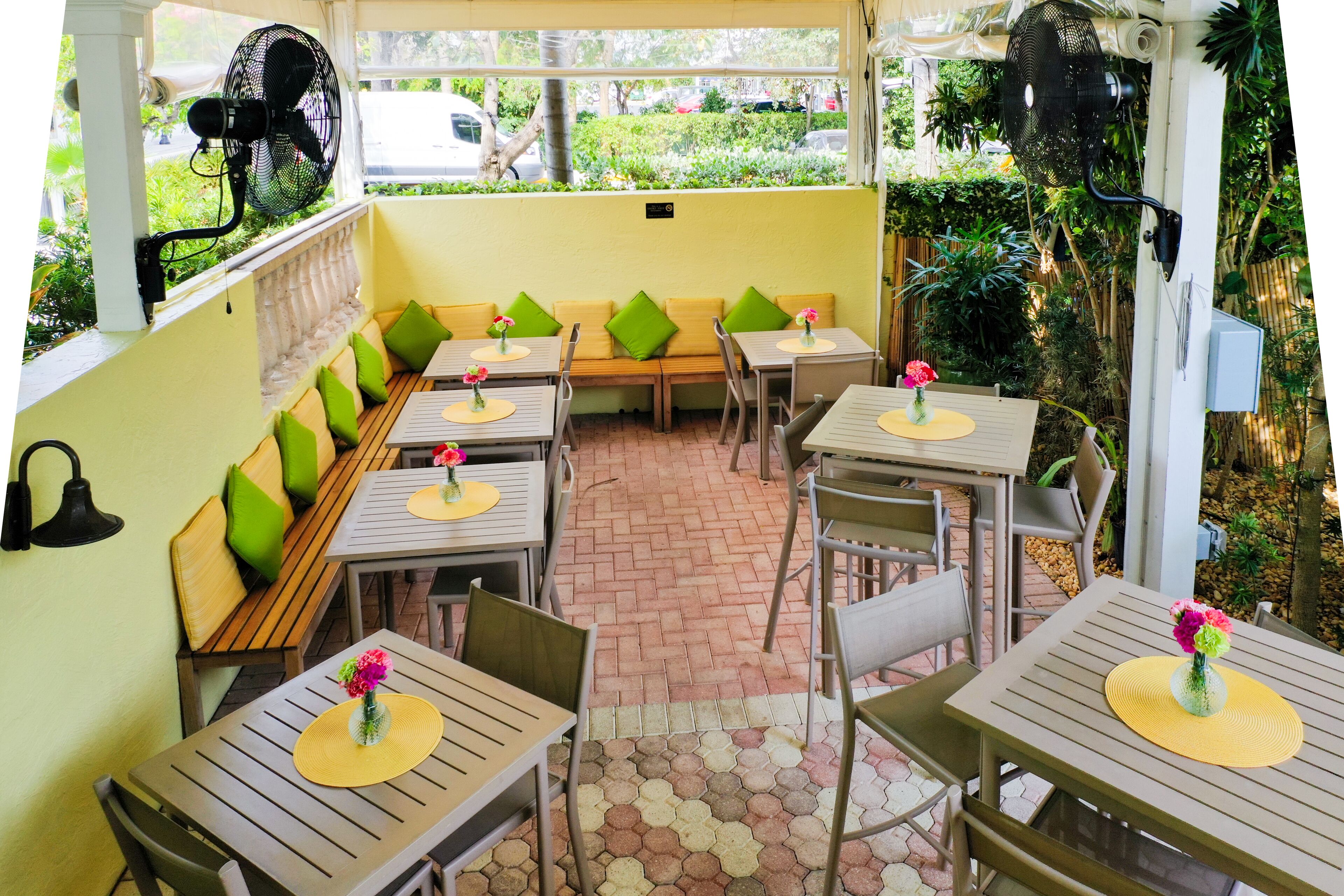 An outdoor cafe with wooden tables, green cushioned benches, and a brick floor.