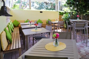 An outdoor patio with wooden tables and benches, some with green cushions.