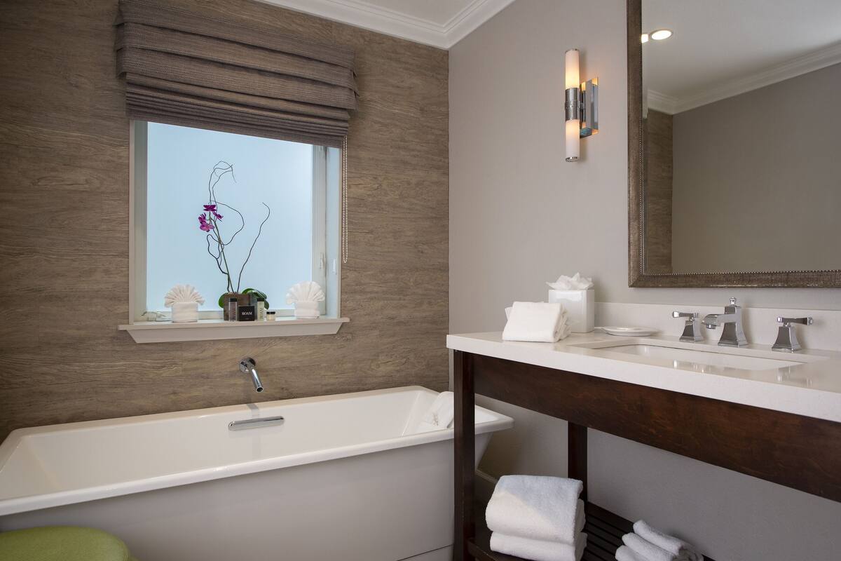 A modern bathroom with a bathtub, a vanity with a mirror, and a window with a view of the sky.