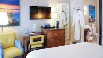 Et hotelværelse med seng, skrivebord med stol, fjernsyn, et maleri og badeværelse med toilet og vask.