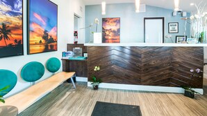A reception area with a wooden herringbone wall, teal chairs, a wooden bench, and two framed sunset paintings. - Almond Tree Inn Hotel - Adults Only (Key West)