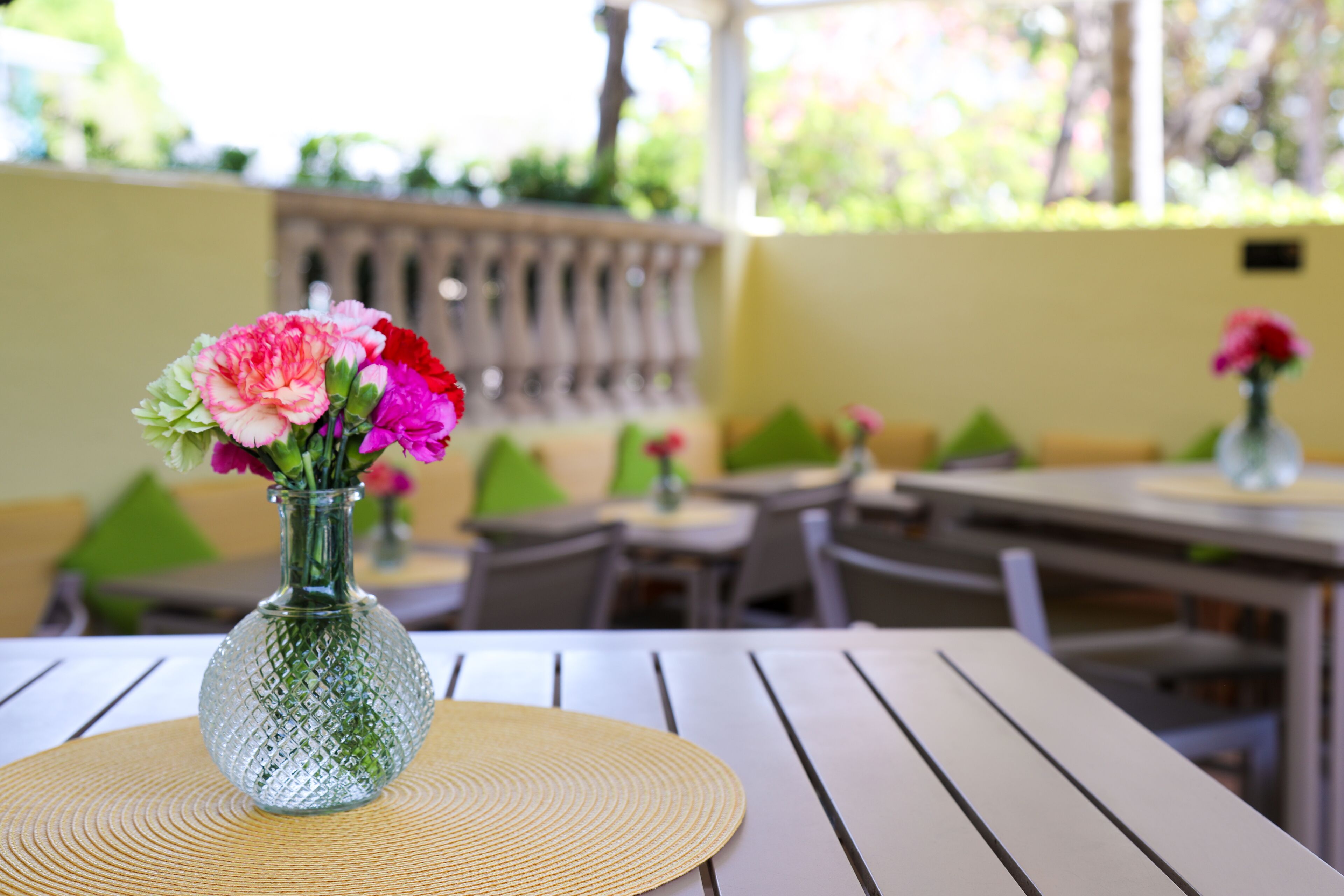 A table with a glass vase containing flowers, set on a woven placemat.