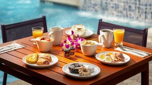 A breakfast table with various food items and drinks, a pool in the background, and a tiled wall. - Almond Tree Inn Hotel - Adults Only (Key West)