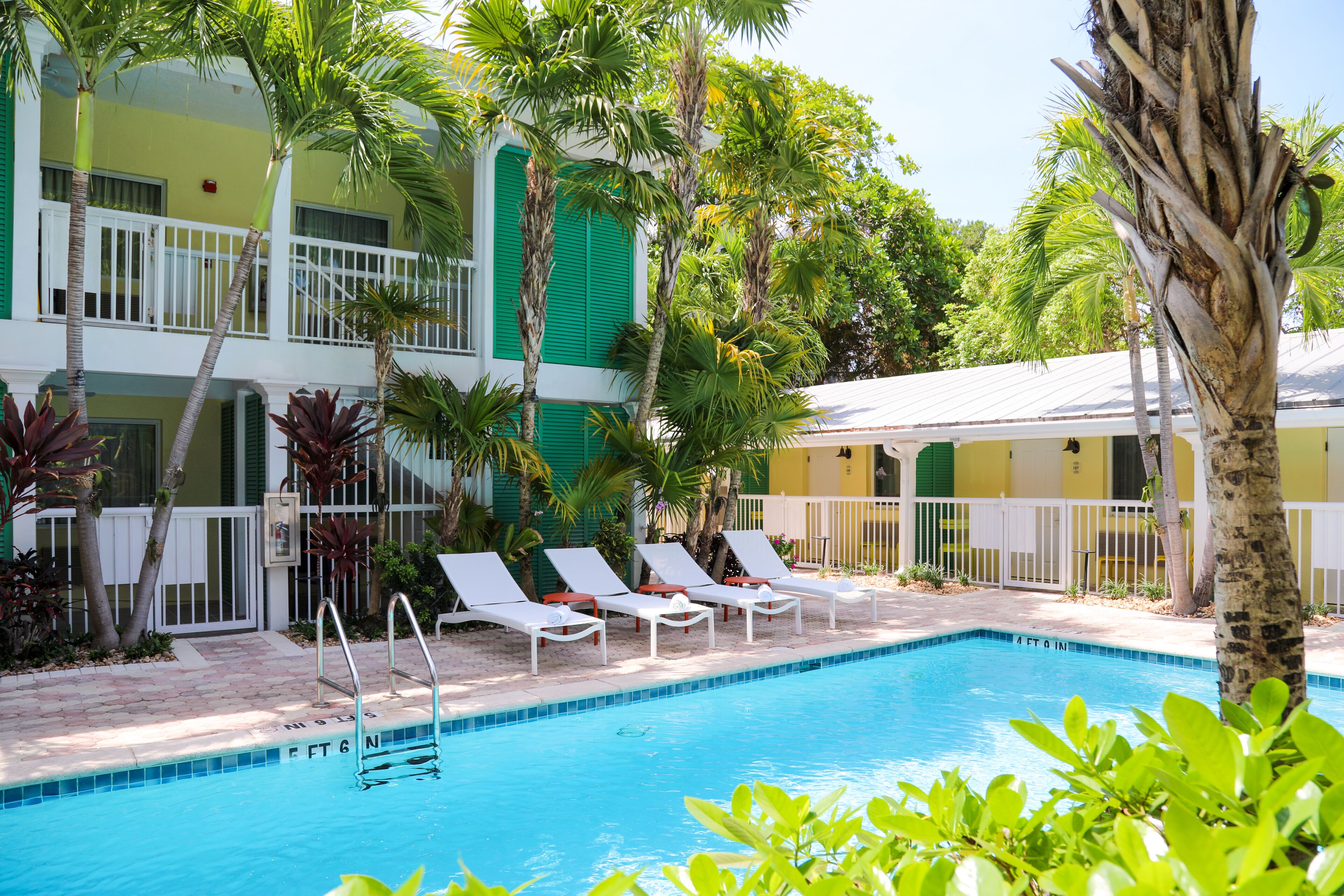 A pool area with lounge chairs, a pool, and a building with balconies and greenery.