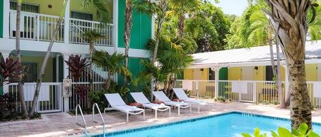 A pool area with lounge chairs, a pool, and a building with balconies and greenery.