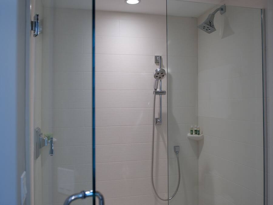 A modern shower with a glass door, a handheld showerhead, and a wall-mounted faucet.