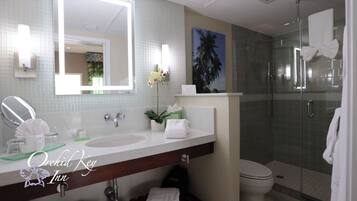 A bathroom with a large mirror, two sinks, a shower, and a toilet.